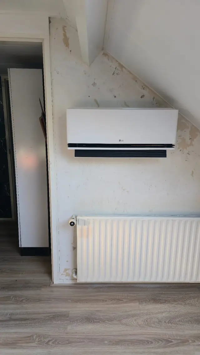 Binnenunit van een LG-airco aan de wand, boven de radiator