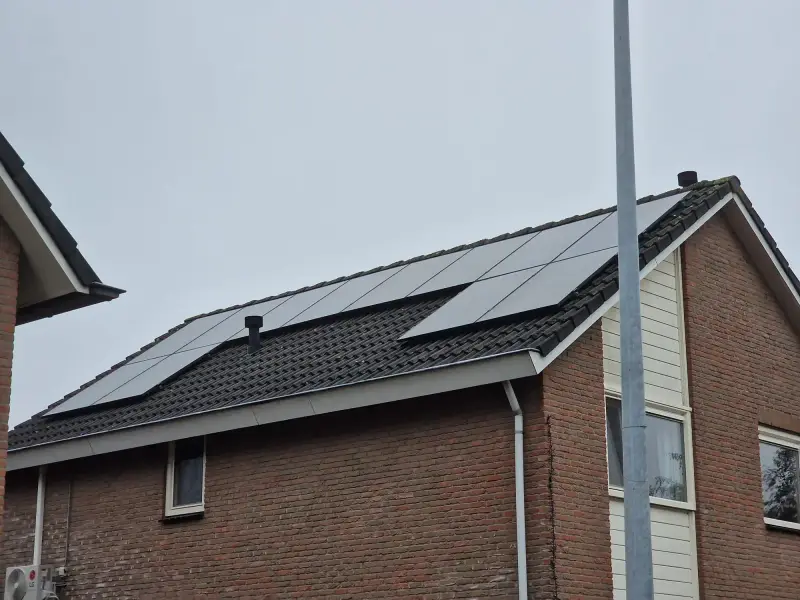 Zwarte zonnepanelen op het dak van een bakstenen woning: met een thuisbatterij bewaar je een deel van die stroom voor de avond
